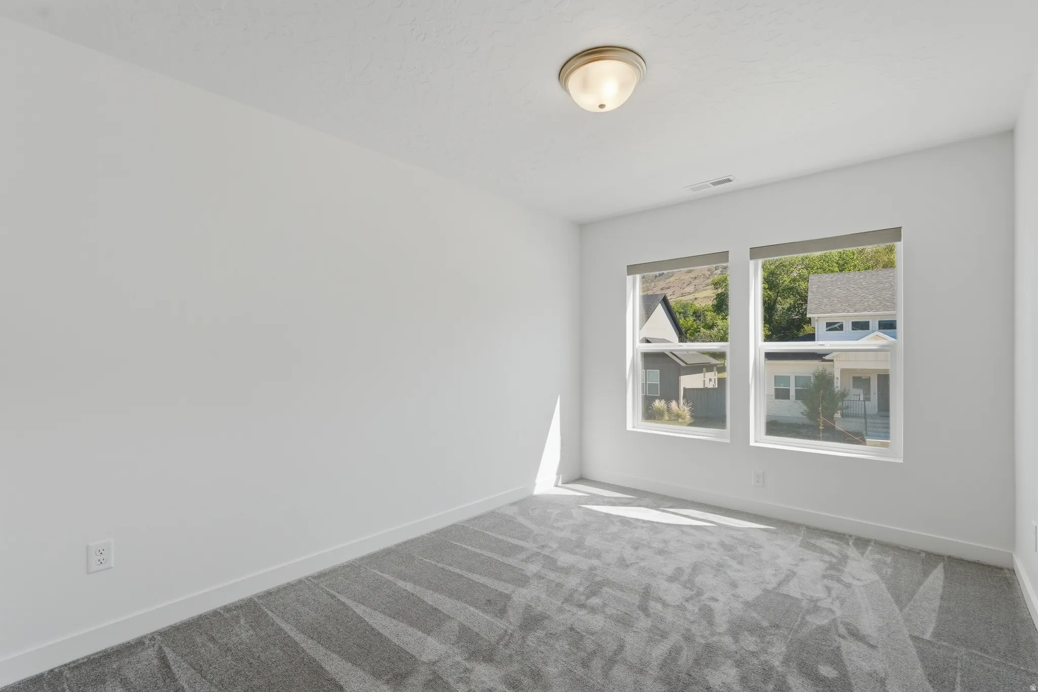 Spacious room featuring dual windows with roller shades, neutral white walls, and a patterned grey carpet