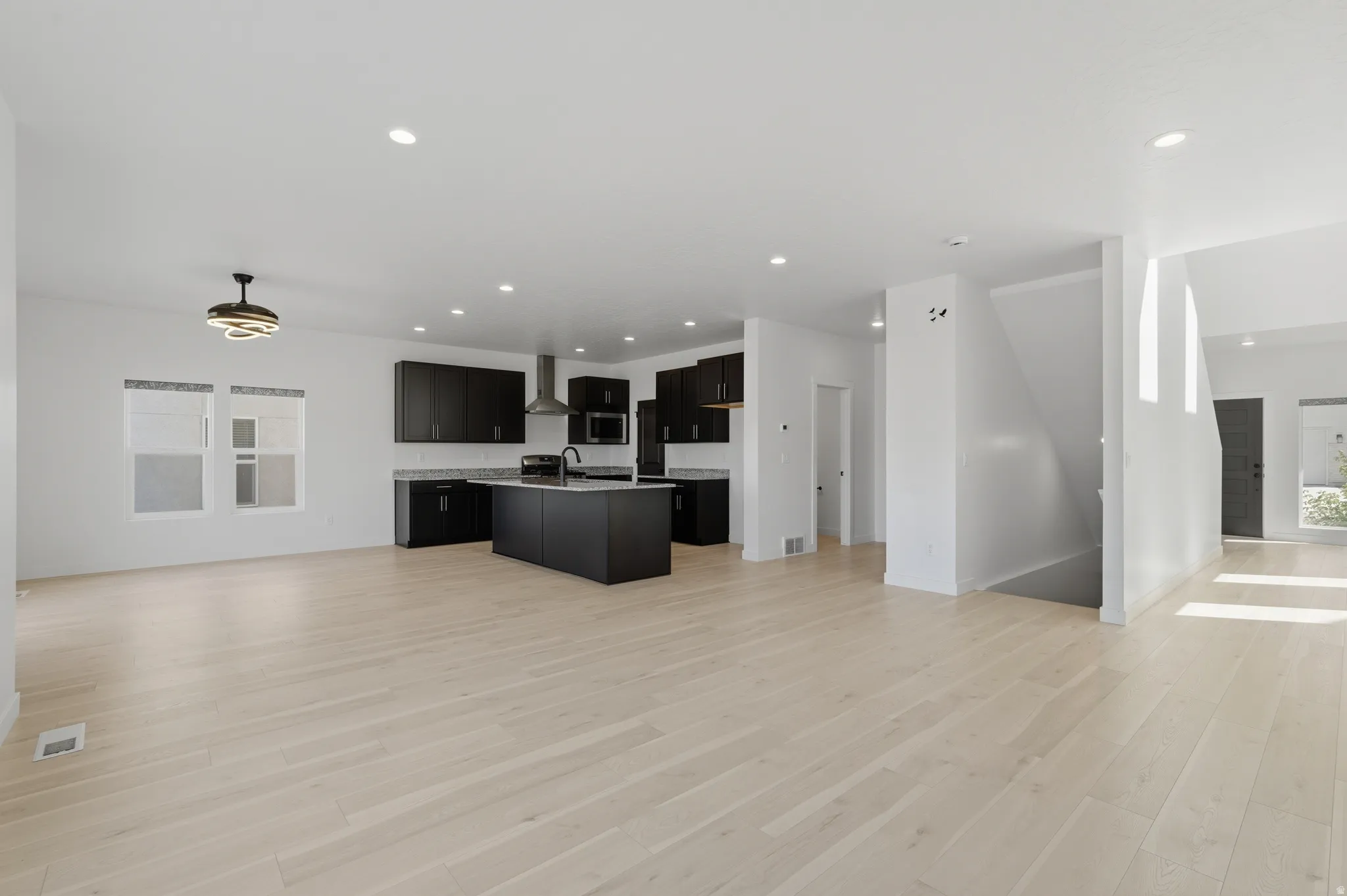 Open-concept living space featuring wood-finish flooring, recessed lighting, and a modern kitchen with dark cabinetry and stainless steel appliances