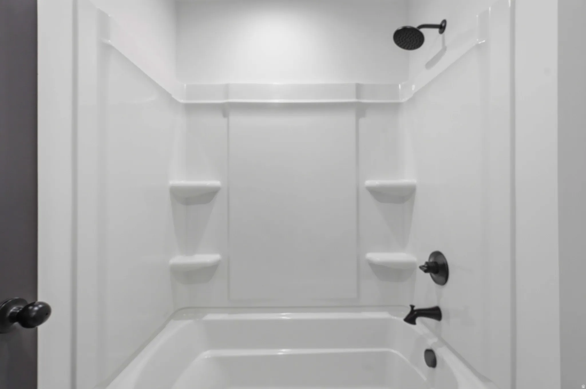 White bathtub and shower combination unit featuring integrated shelving and matte black fixtures