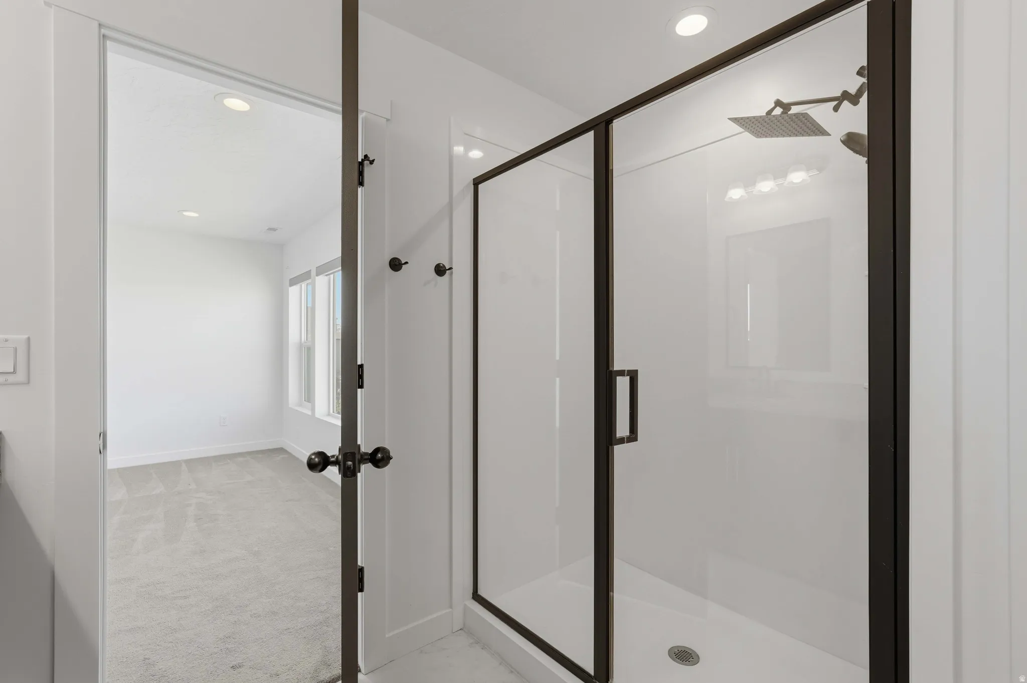 Walk-in shower with dark-framed glass enclosure, square rain shower head, and recessed lighting