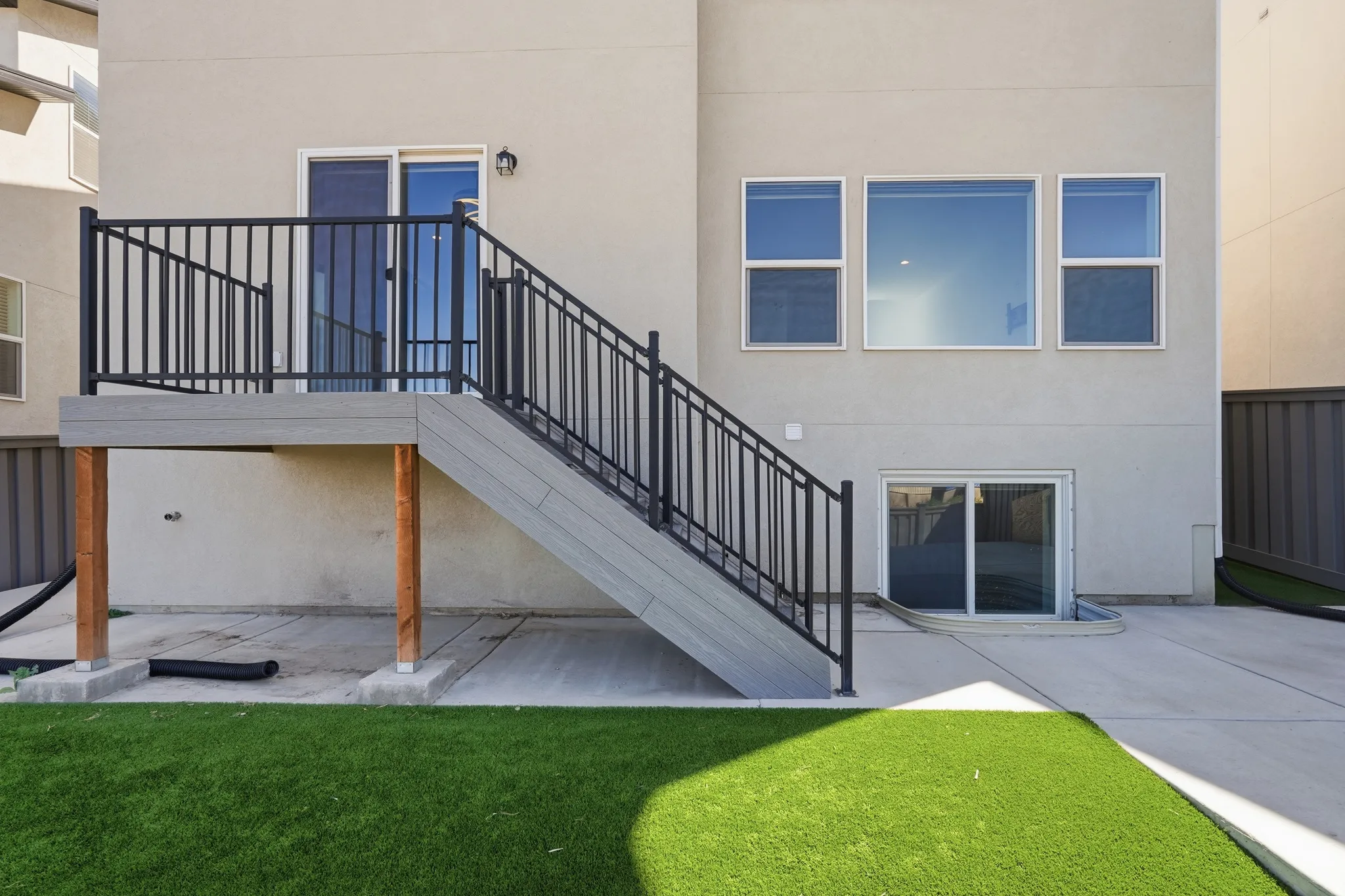 Rear exterior with a composite deck featuring black metal railings, a sliding glass door, and a lower-level concrete patio with a walk-out basement entrance