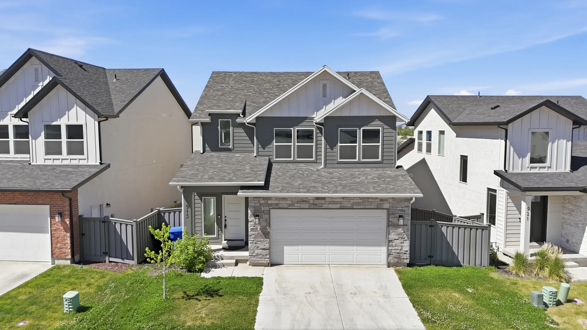 Modern-style home featuring a stone and siding facade, an attached two-car garage, multiple windows with dark framing, and a front entry with a white door