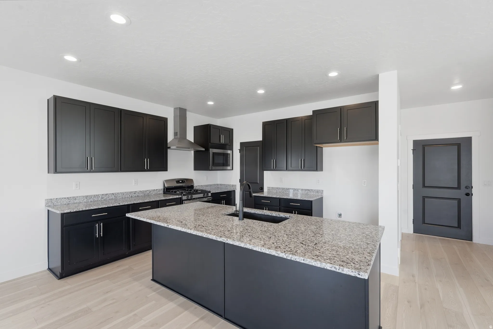Modern kitchen featuring dark cabinetry, speckled countertops, stainless steel appliances, and wood-finish flooring