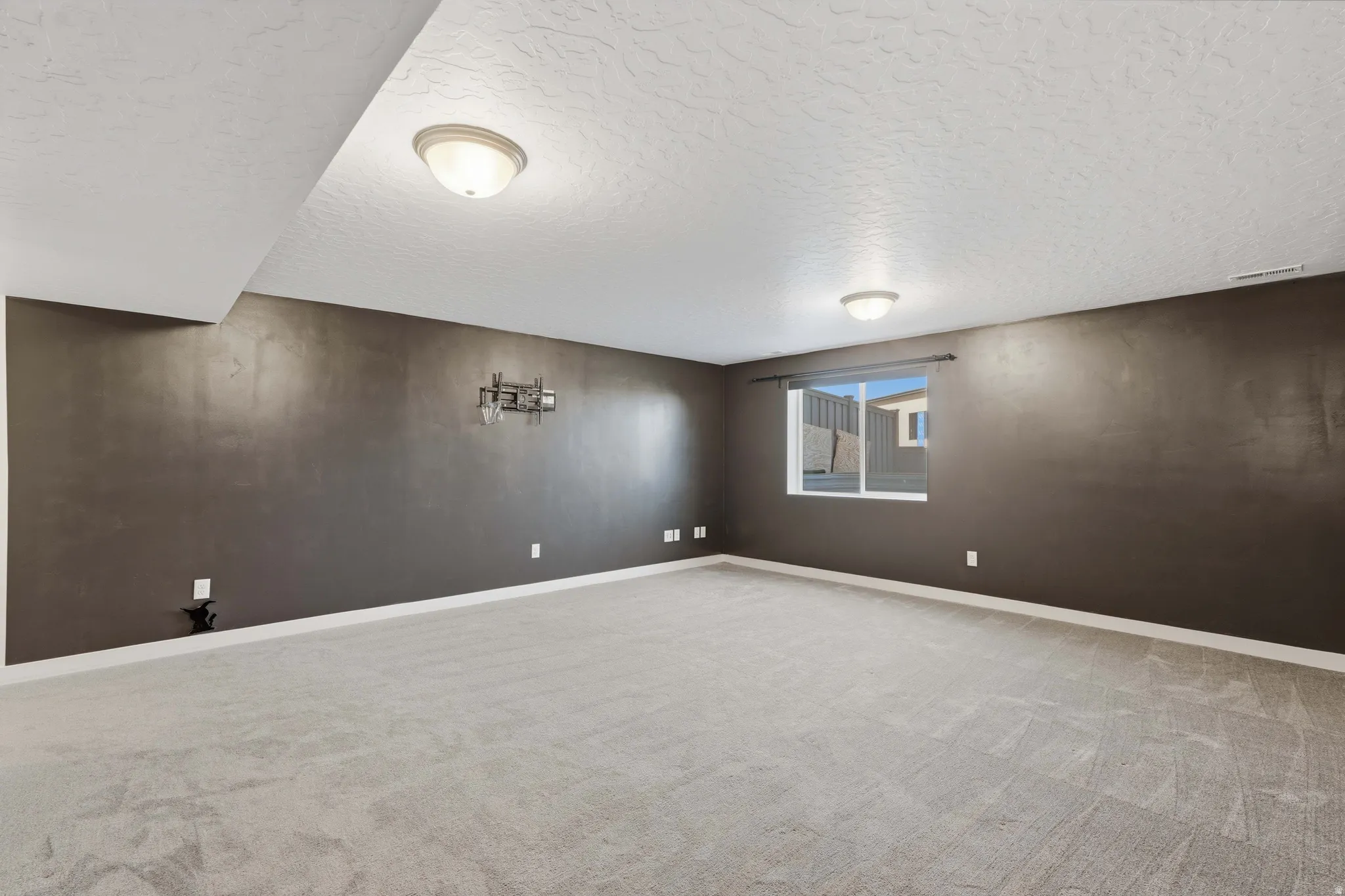 Spacious room featuring neutral carpeting, a large window, and overhead flush-mount lighting fixtures