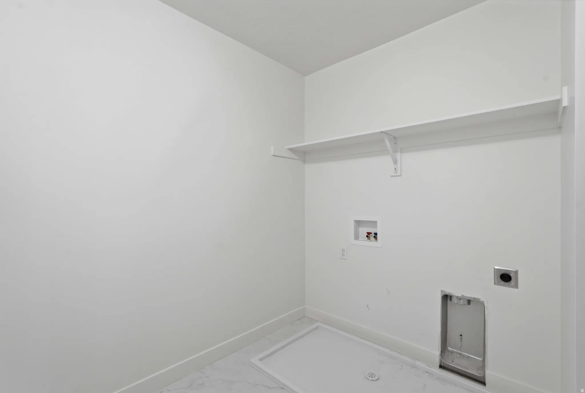 Dedicated laundry area featuring a white floating shelf, wall-mounted utility connections, and tile flooring