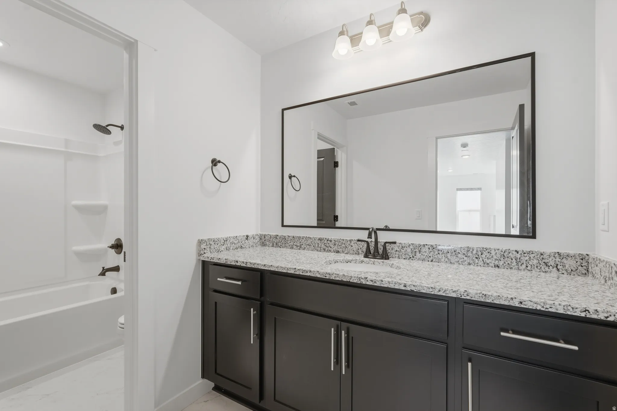 Bathroom featuring a spacious vanity with black cabinetry, a light speckled countertop, and a large framed mirror