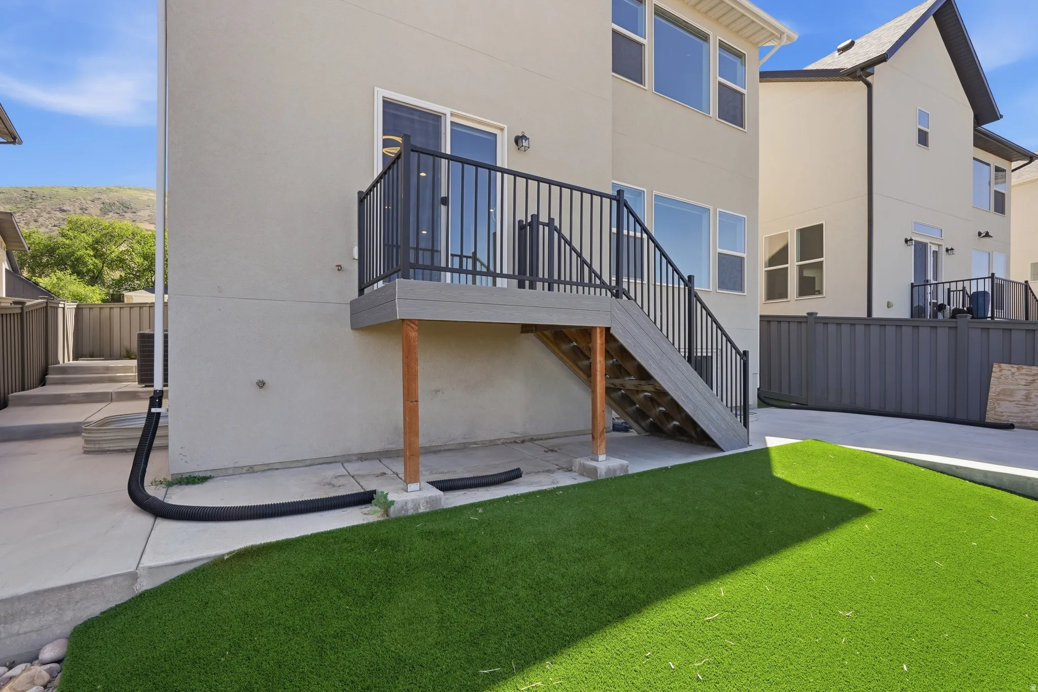 Rear exterior featuring a composite deck with black metal railings, a sliding glass door, multiple large windows, and a lower-level patio with artificial turf