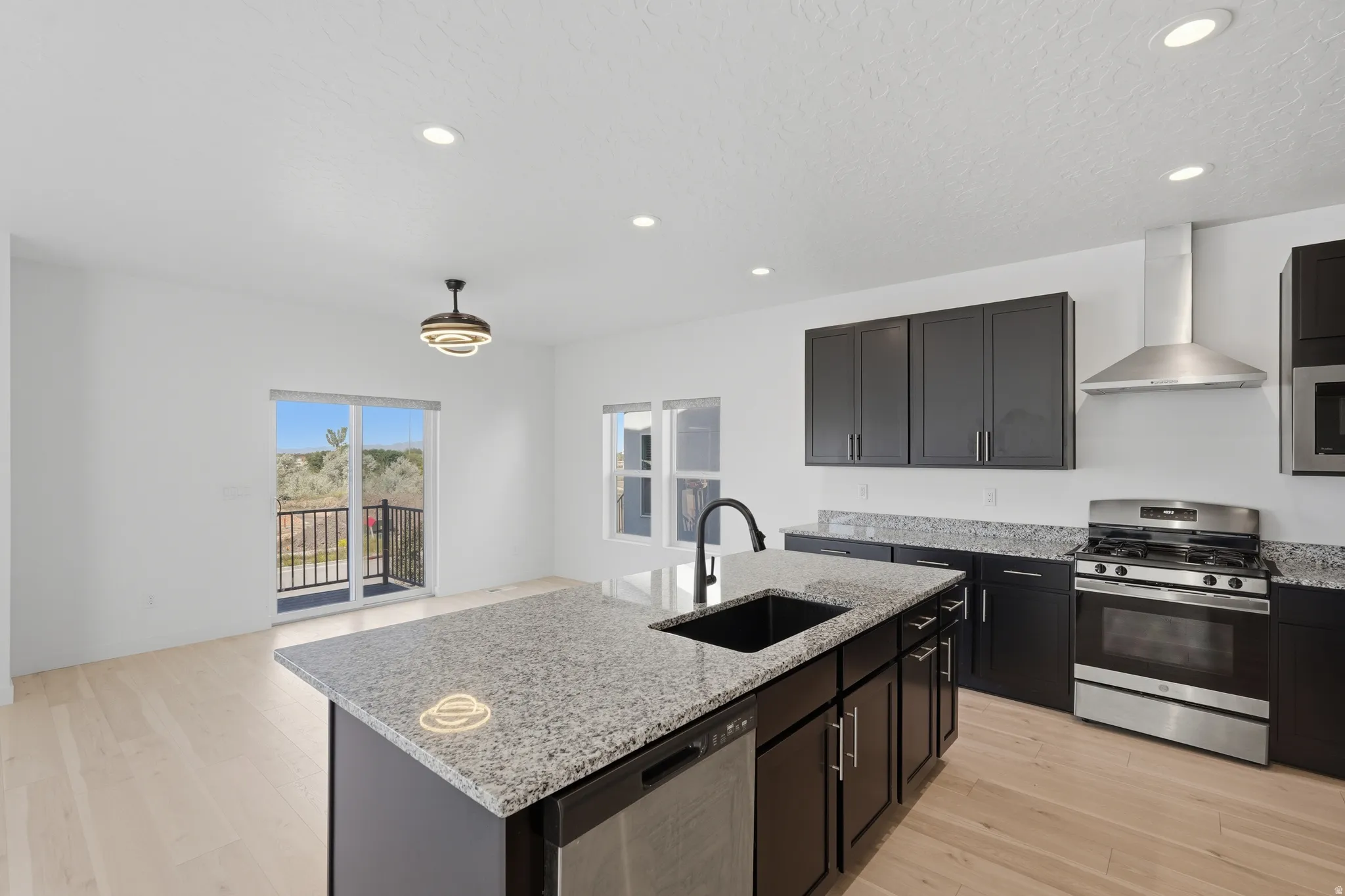 Open-concept kitchen featuring an island with granite countertops and an undermount sink, dark wood-finish cabinetry, stainless steel appliances, and light wood-finish flooring