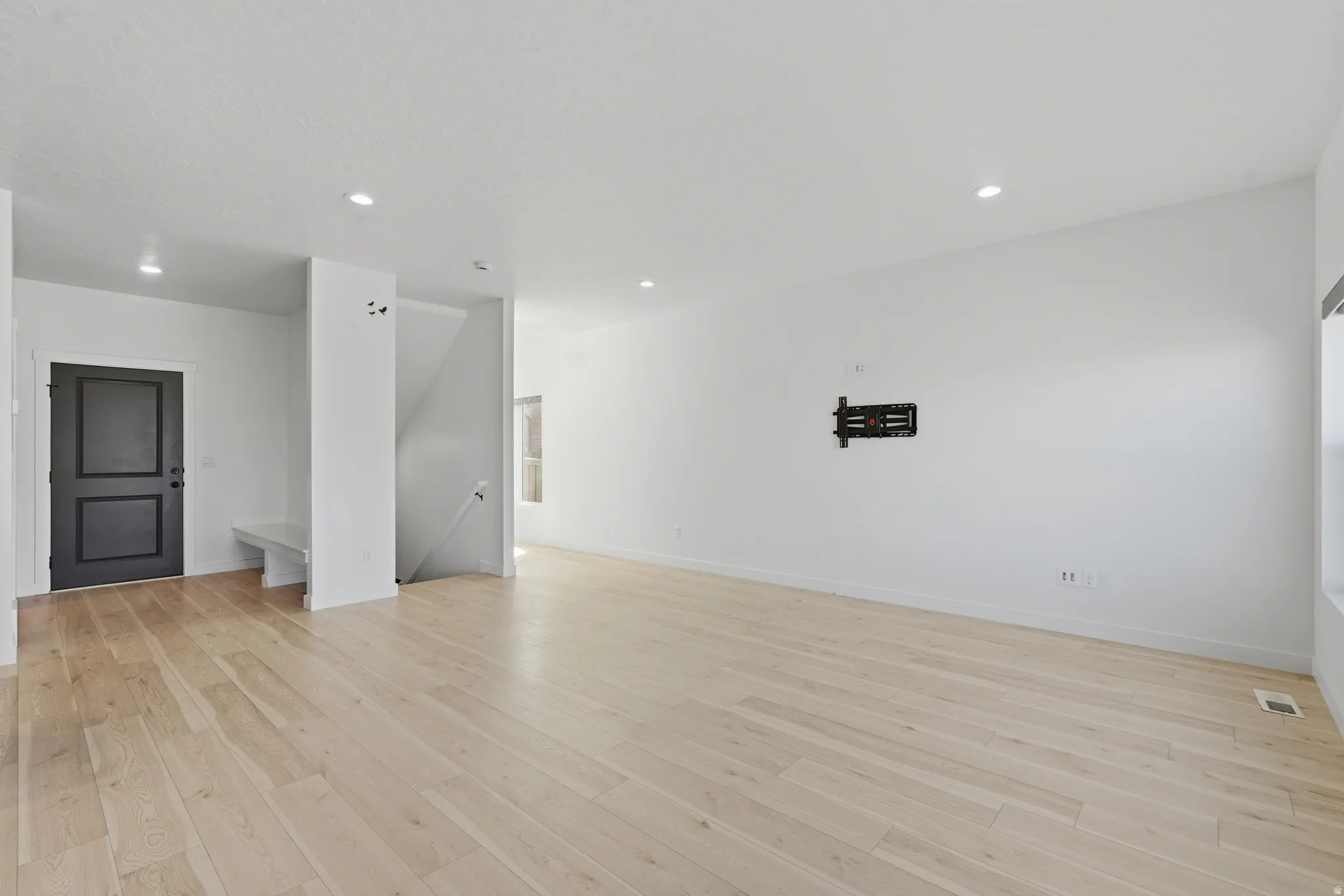 Open-concept living area featuring light wood-finish flooring, recessed lighting, a built-in entry bench, and a dark paneled entry door