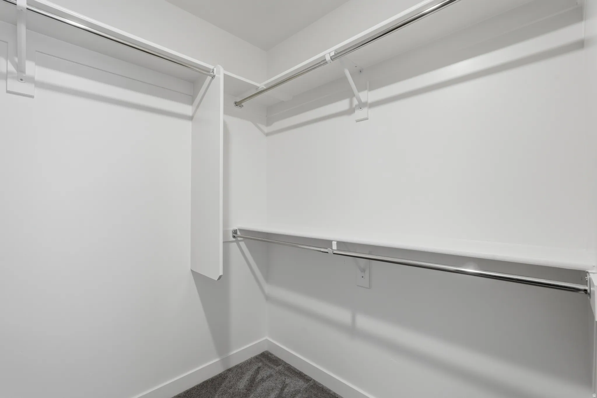 Walk-in closet with white walls, white shelving, and chrome hanging rods