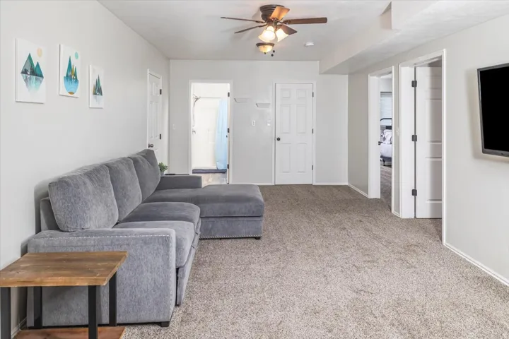 Carpeted living area featuring a ceiling fan with integrated lighting, a wall-mounted television, and multiple white panel doors