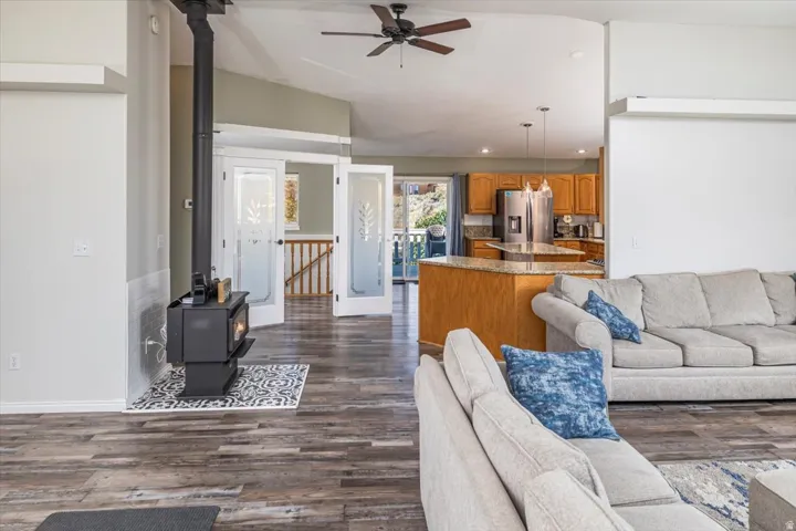 Vaulted ceiling living area featuring a black wood-burning stove, wood-finish flooring, and double glass-paneled doors with etched patterns