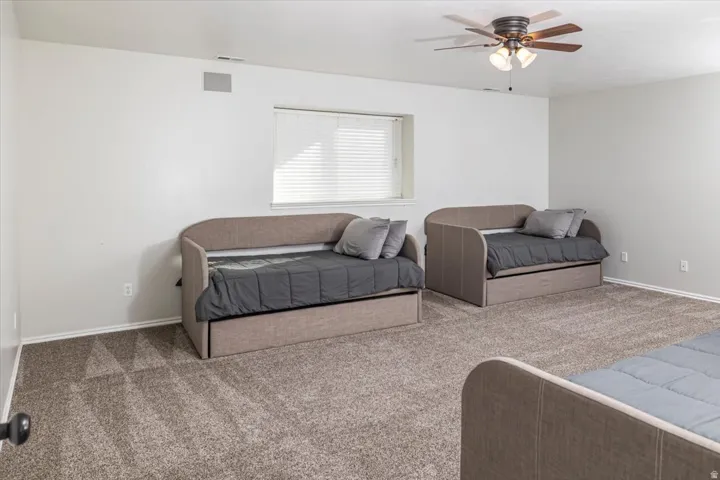Spacious room with plush carpet flooring, a ceiling fan with integrated lighting, and a window with blinds