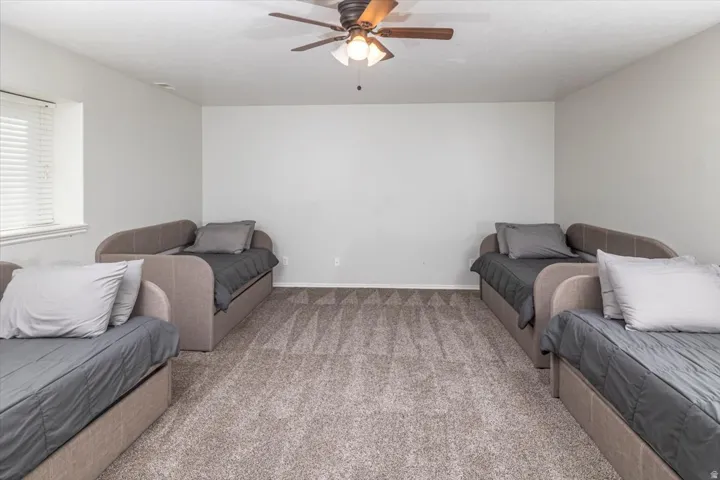 Spacious room with light neutral wall paint, textured carpet flooring, a ceiling fan with integrated lighting, and a window featuring horizontal blinds