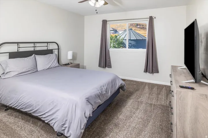 Carpeted room featuring a ceiling fan, a window with curtains, and a light-toned wood-finish dresser
