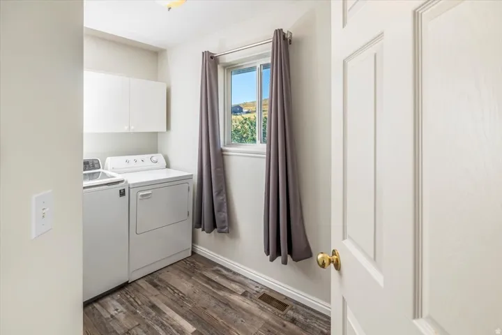 Dedicated laundry area featuring wood-finish flooring, overhead cabinetry, and a window with exterior views