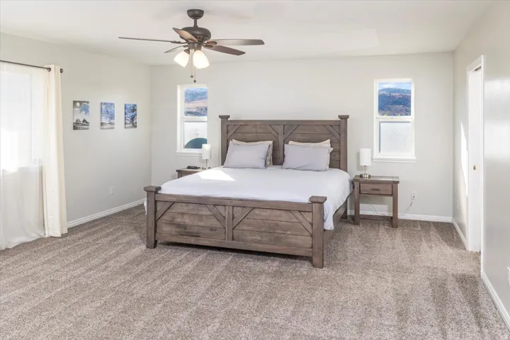 Spacious bedroom featuring neutral carpeting, a ceiling fan, and multiple windows providing natural light