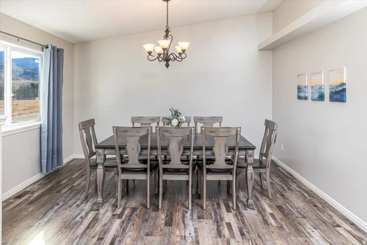 Dining area featuring wood-finish flooring, a large window, a classic chandelier fixture, and vaulted ceilings