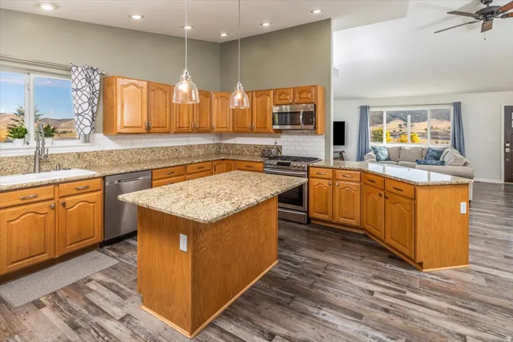 Open-concept kitchen featuring wood-finish cabinetry, granite countertops, stainless steel appliances, and a central island