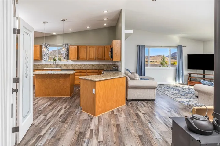 Open-concept living space featuring wood-finish flooring, vaulted ceilings, and a kitchen with wood cabinetry and granite countertops