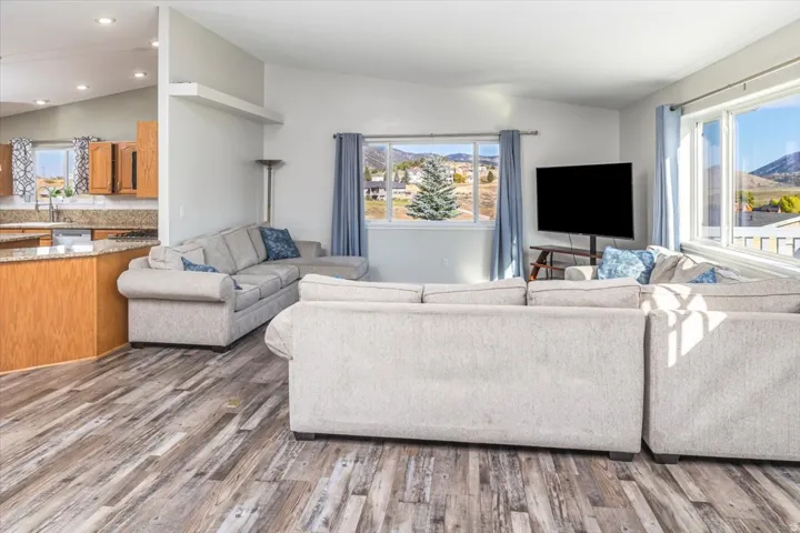 Open-concept living area featuring wood-finish flooring, vaulted ceilings, and large windows