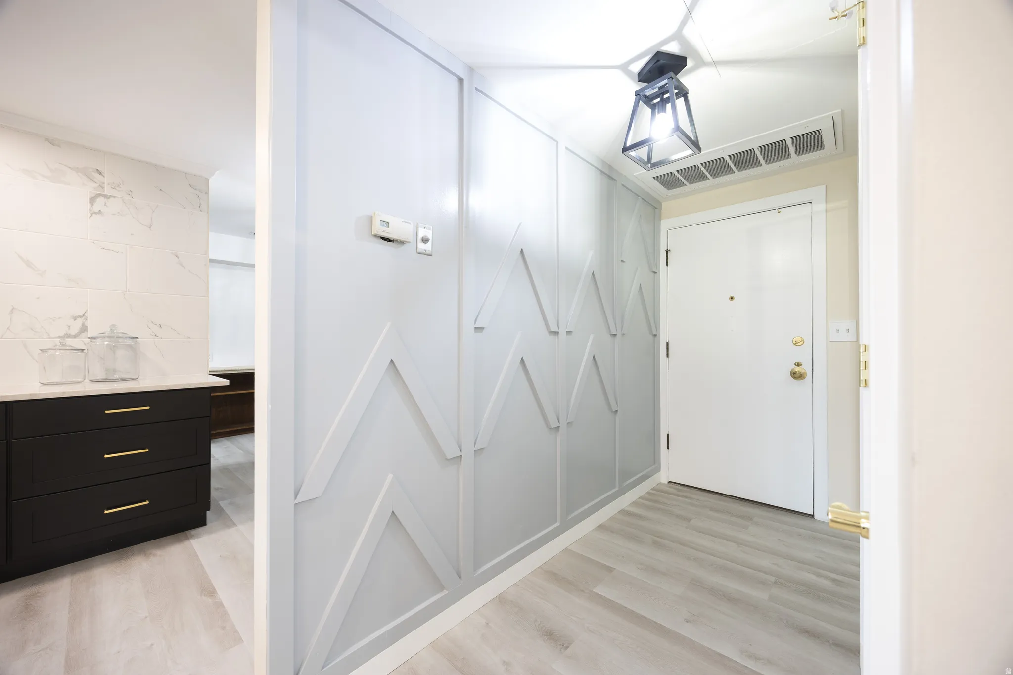 Entryway featuring decorative wainscoting paneling, light wood-finish flooring, and a contemporary ceiling light fixture