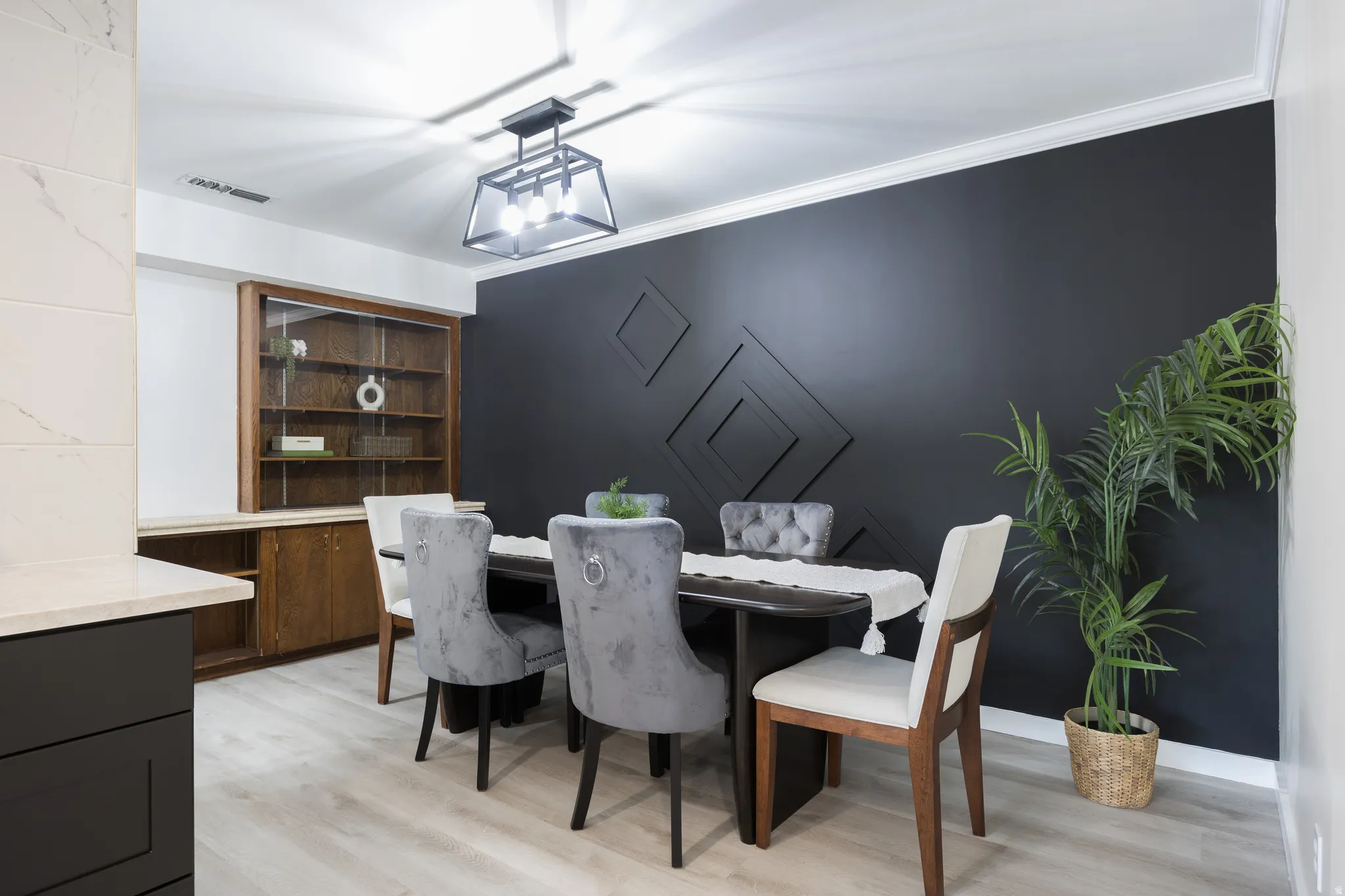 Dining area featuring a dark accent wall with geometric paneling, wood-finish flooring, and a contemporary ceiling light fixture