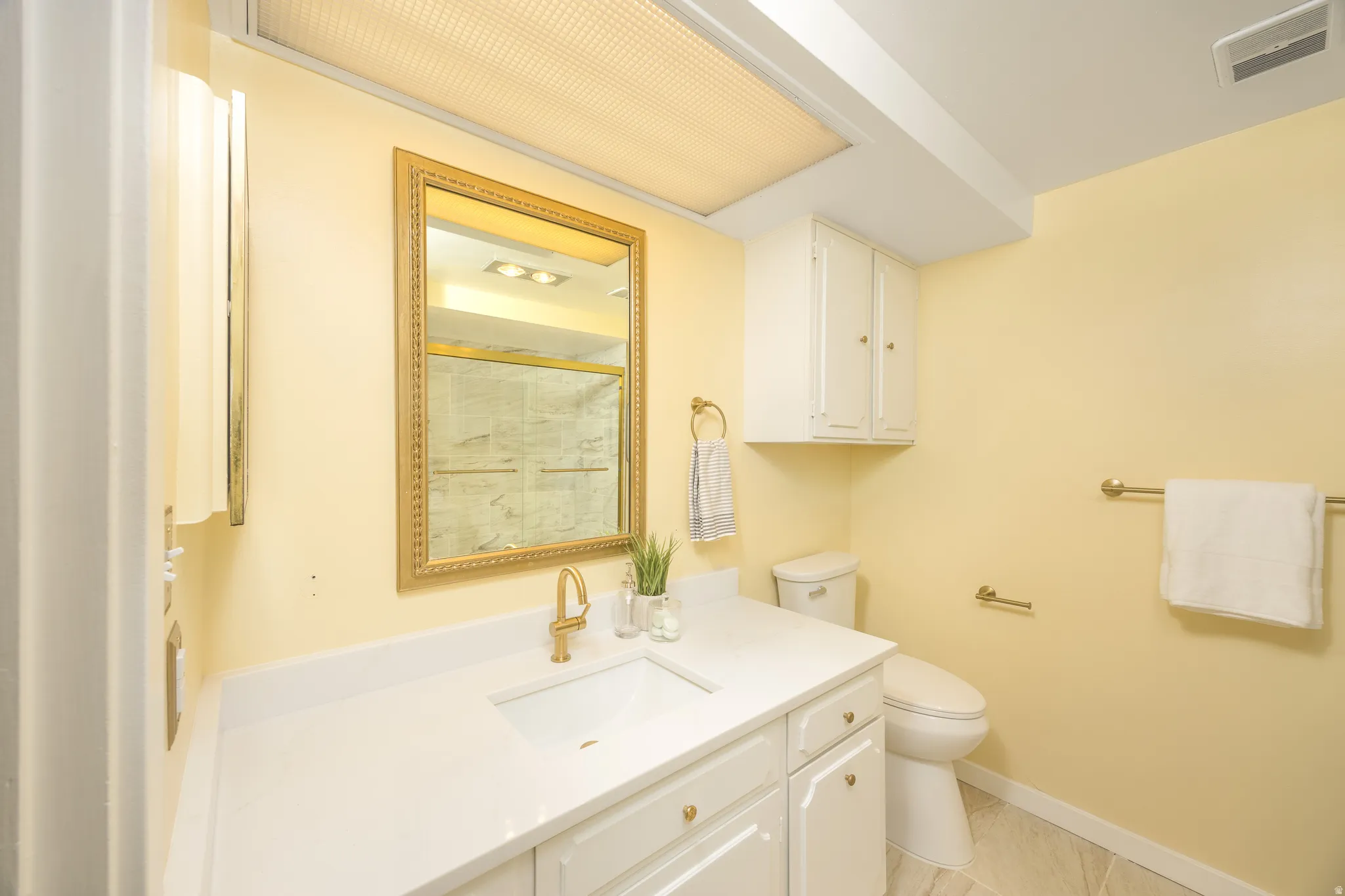 Bathroom featuring a white vanity with an integrated sink, gold-finish faucet, and a decorative framed mirror