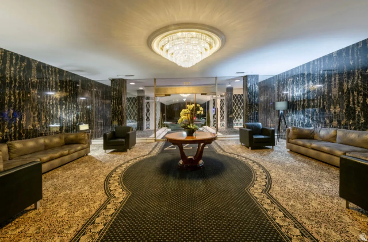 Grand entry foyer featuring a large chandelier, dark patterned wall coverings, and intricate patterned carpeting