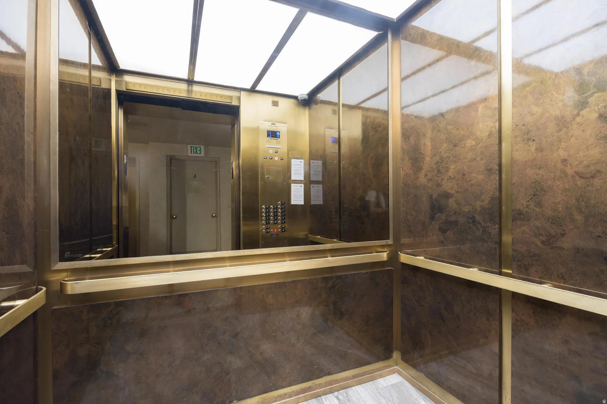 Elevator interior featuring brass accents, full-height mirror, stone-finish walls, and wood-finish flooring