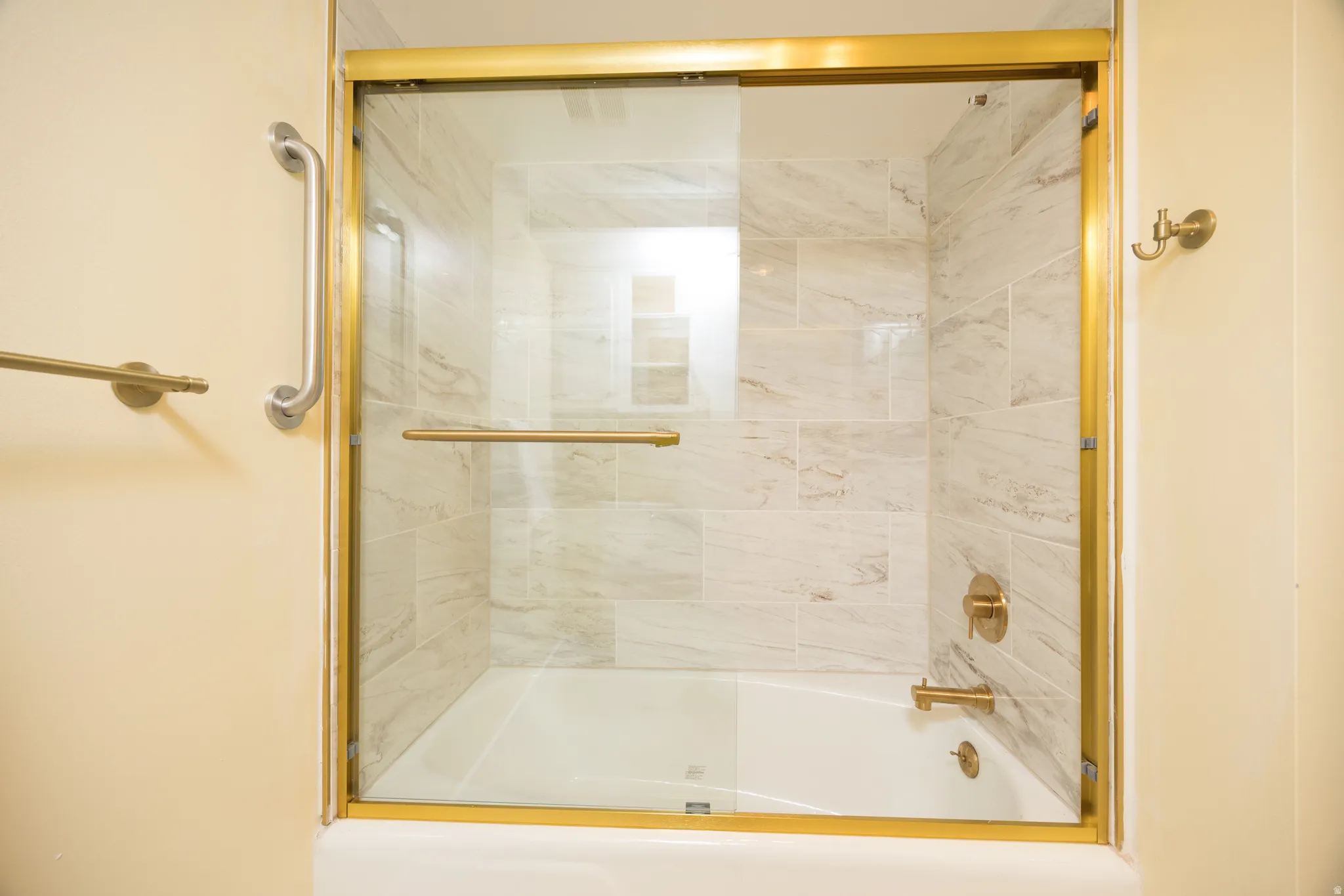 Tub-shower combination featuring a gold-finish framed glass enclosure, light-toned tile surround, and coordinating gold-finish fixtures
