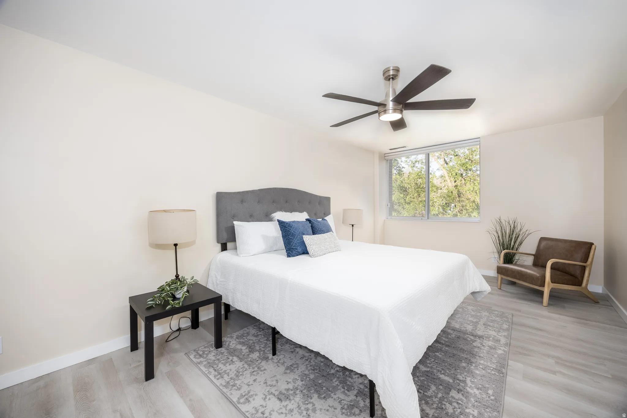 Spacious bedroom featuring light-toned flooring, a large window, a ceiling fan, and neutral wall paint