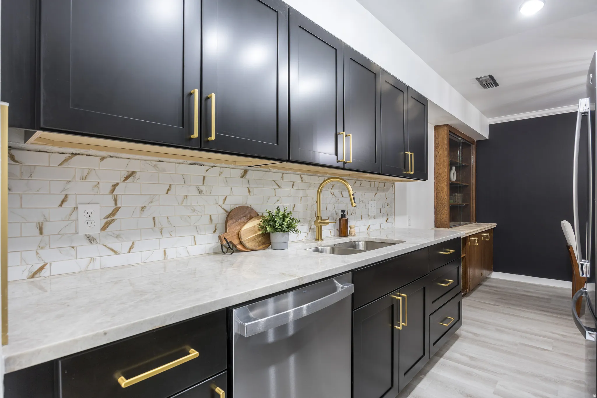 Modern kitchen featuring black cabinetry with gold-tone hardware, a stainless steel undermount sink, a gold-tone faucet, light-toned countertops, and a subway tile backsplash