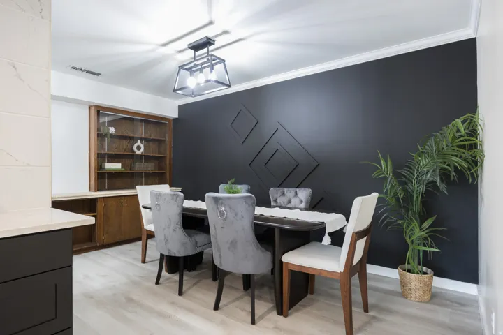 Dining area featuring a dark accent wall with geometric paneling, wood-finish flooring, and a contemporary ceiling light fixture