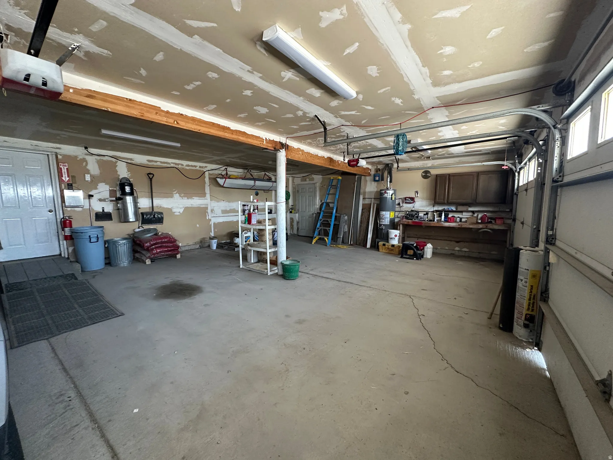 Spacious garage featuring a concrete floor, overhead fluorescent lighting, an automatic garage door opener, built-in cabinetry, and a workbench area