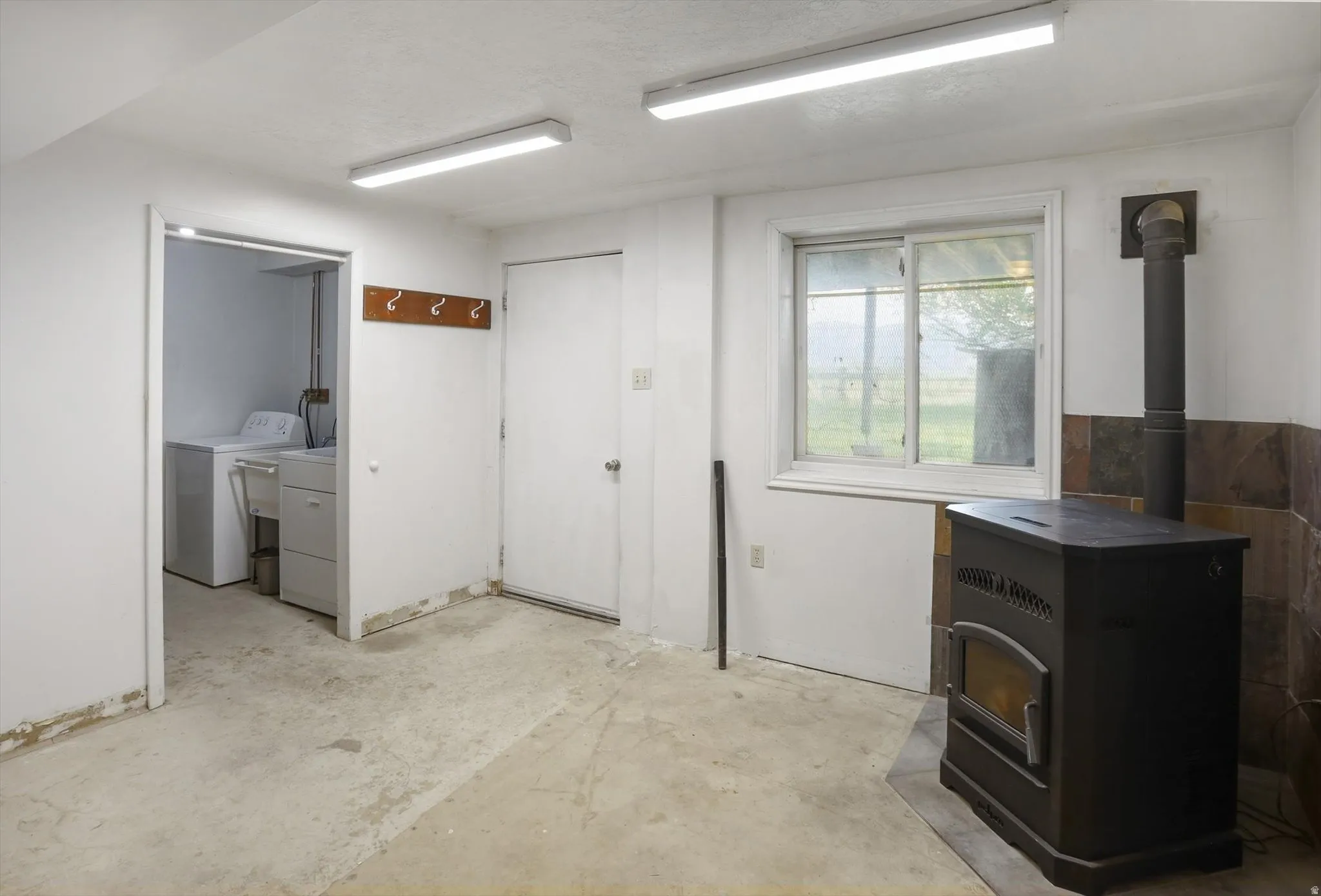 Functional utility room featuring a window, built-in wood stove on a tiled hearth, and a dedicated laundry area with a utility sink