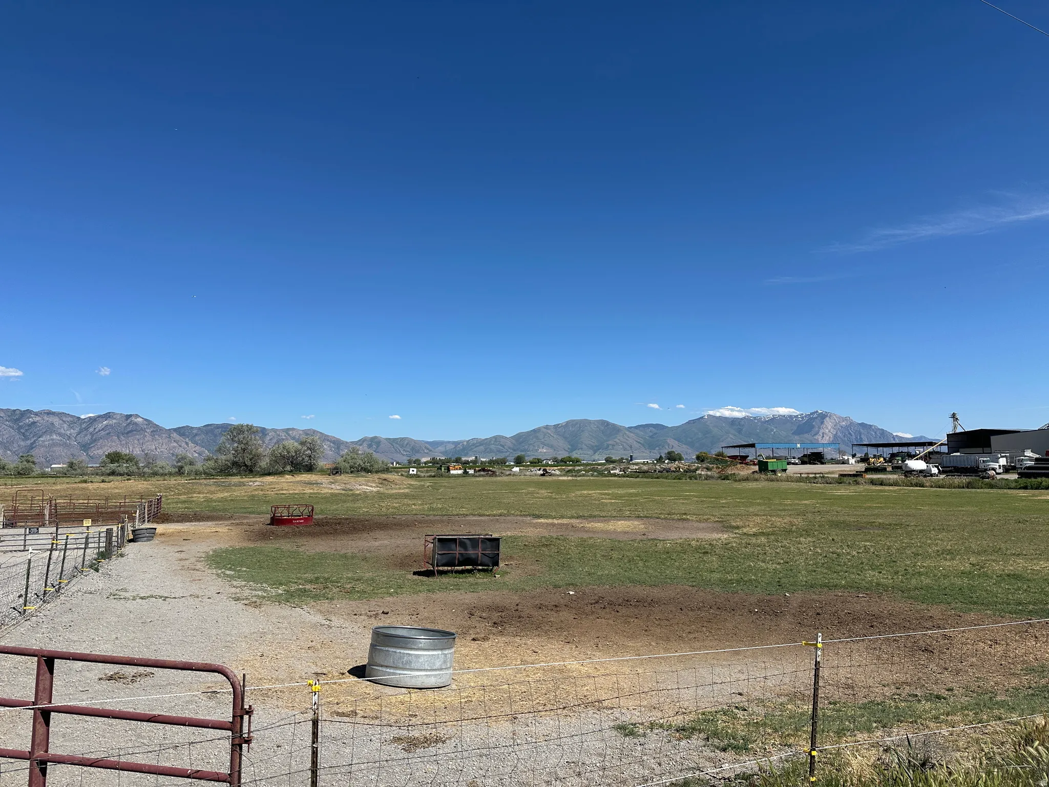 Expansive open field with partial fencing and a galvanized trough, set against a backdrop of distant mountains
