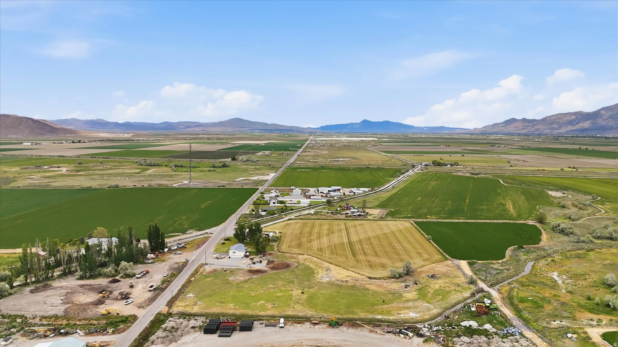 Expansive agricultural land featuring a mix of green fields and tilled acreage, with a winding creek and distant mountain ranges