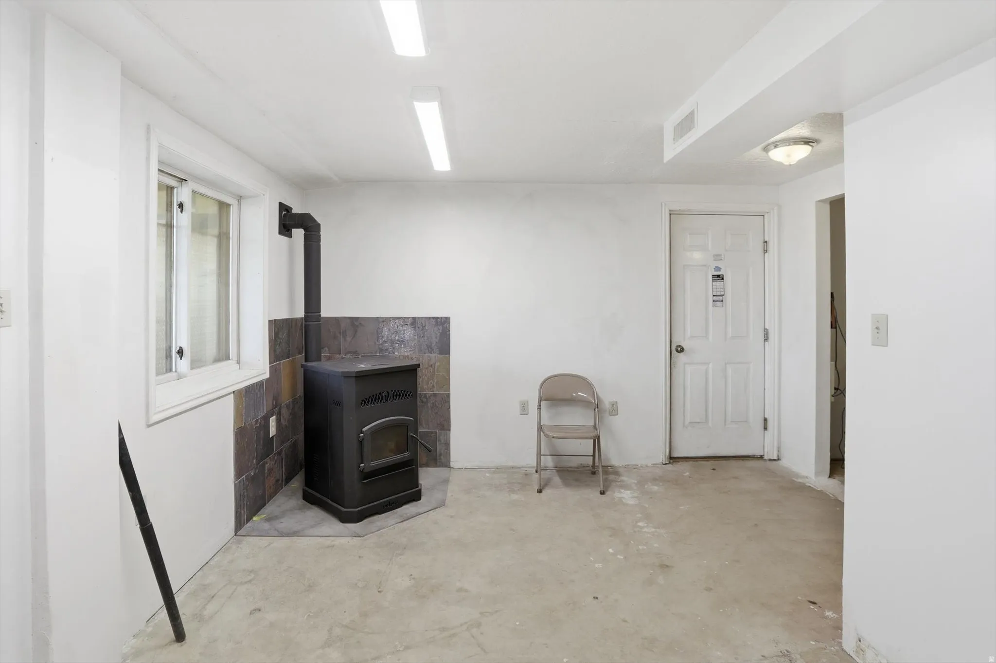 Room featuring a black wood-burning stove with a slate tile surround, a single window, and concrete flooring