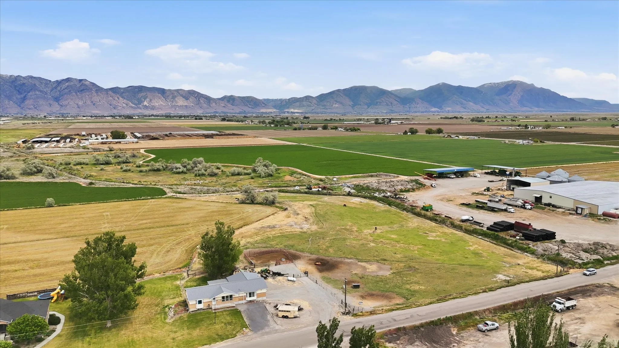 Aerial property view with expansive agricultural fields, distant mountains and multiple outbuildings