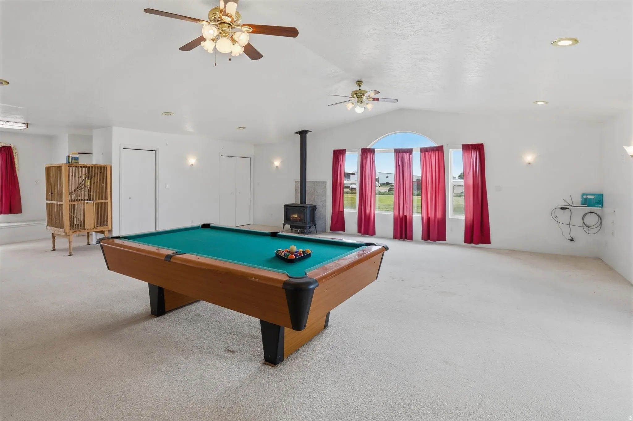 Spacious room featuring vaulted ceilings, a wood-burning stove, and multiple windows with an arched transom