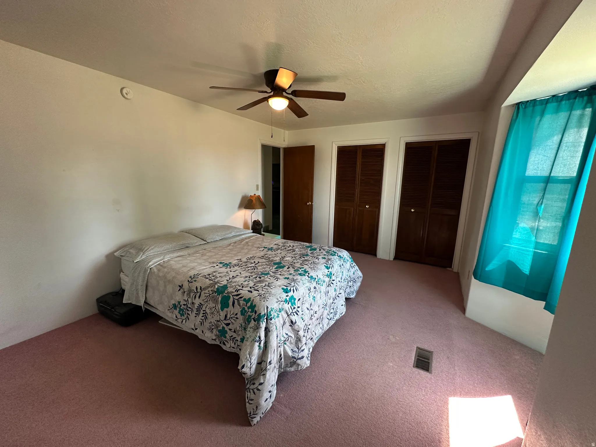 Room featuring wall-to-wall carpeting, a ceiling fan with integrated lighting, a window with a sill, and two built-in closets with bi-fold doors
