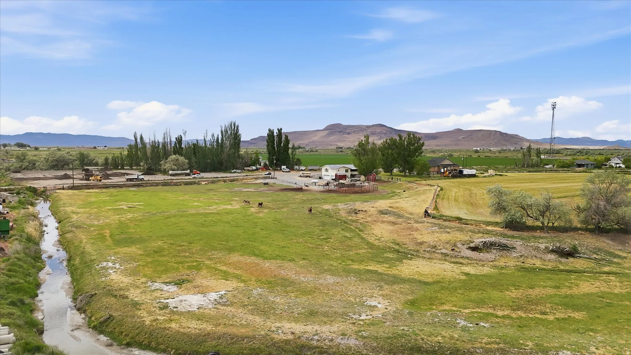 Expansive rural property featuring a residential structure with a red roof, multiple outbuildings, and extensive open land