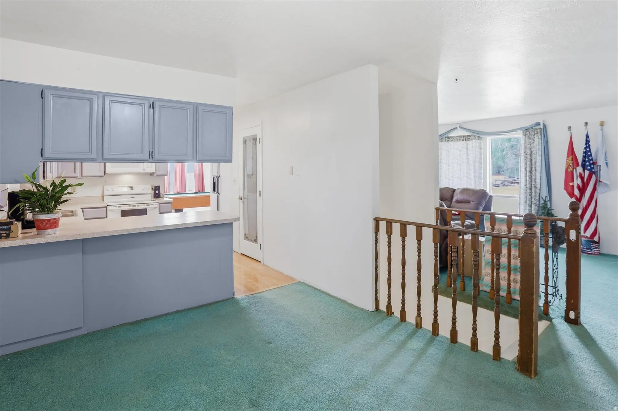 Kitchen with blue cabinetry and white appliances, featuring a peninsula with a light-toned countertop