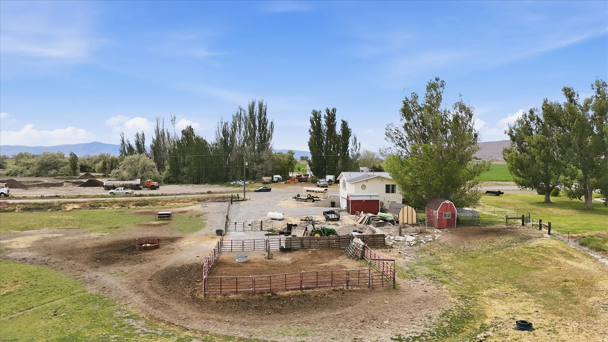 Spacious rural property featuring a primary residence with an attached garage, a red storage shed, and multiple fenced animal enclosures