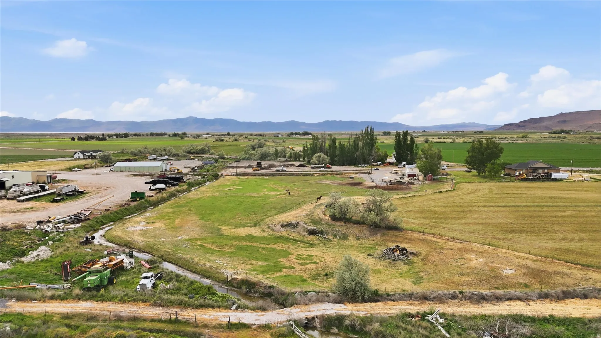 Expansive agricultural property featuring multiple structures, open fields, and mountain backdrops