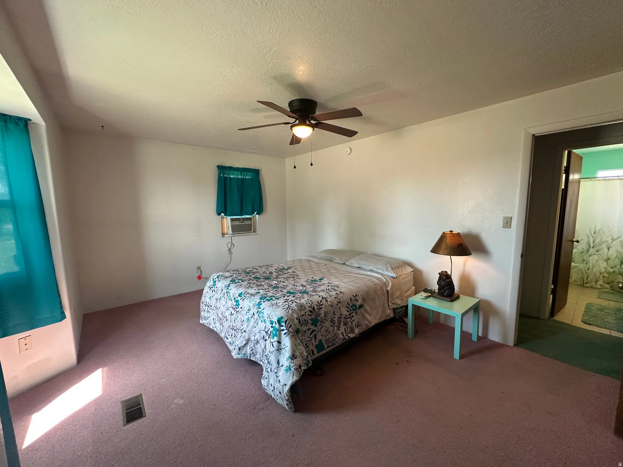Carpeted room featuring a ceiling fan with integrated lighting, two windows with teal curtains, and a wall-mounted air conditioning unit