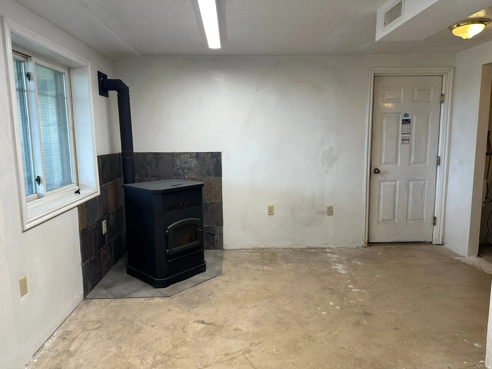 Interior space featuring a black freestanding stove with a slate tile surround, a single window, and concrete flooring