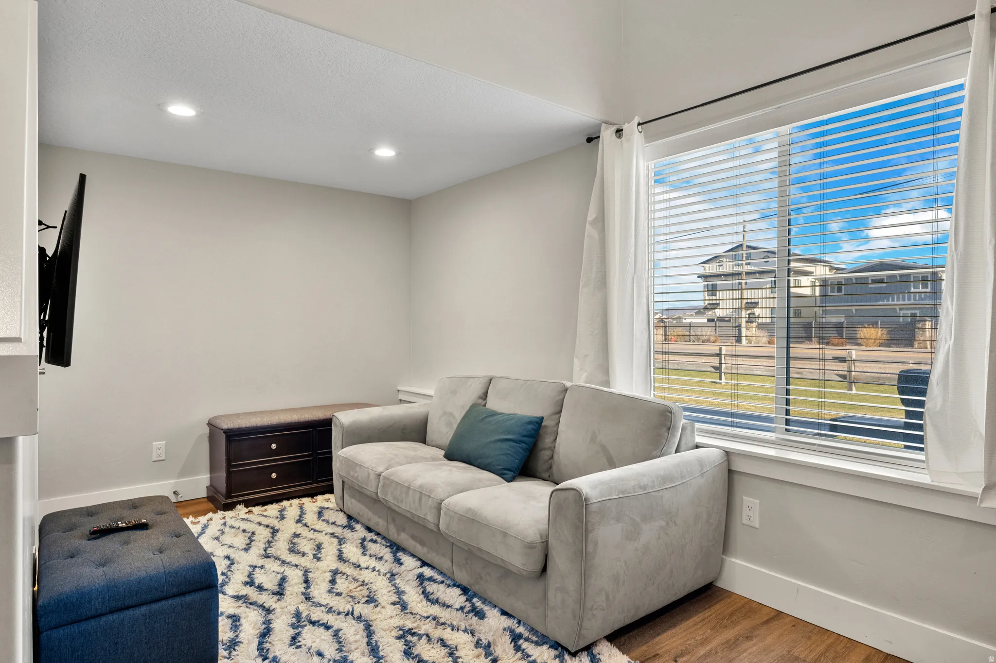 Living space featuring recessed lighting, a large window with blinds and curtains, and wood-finish flooring