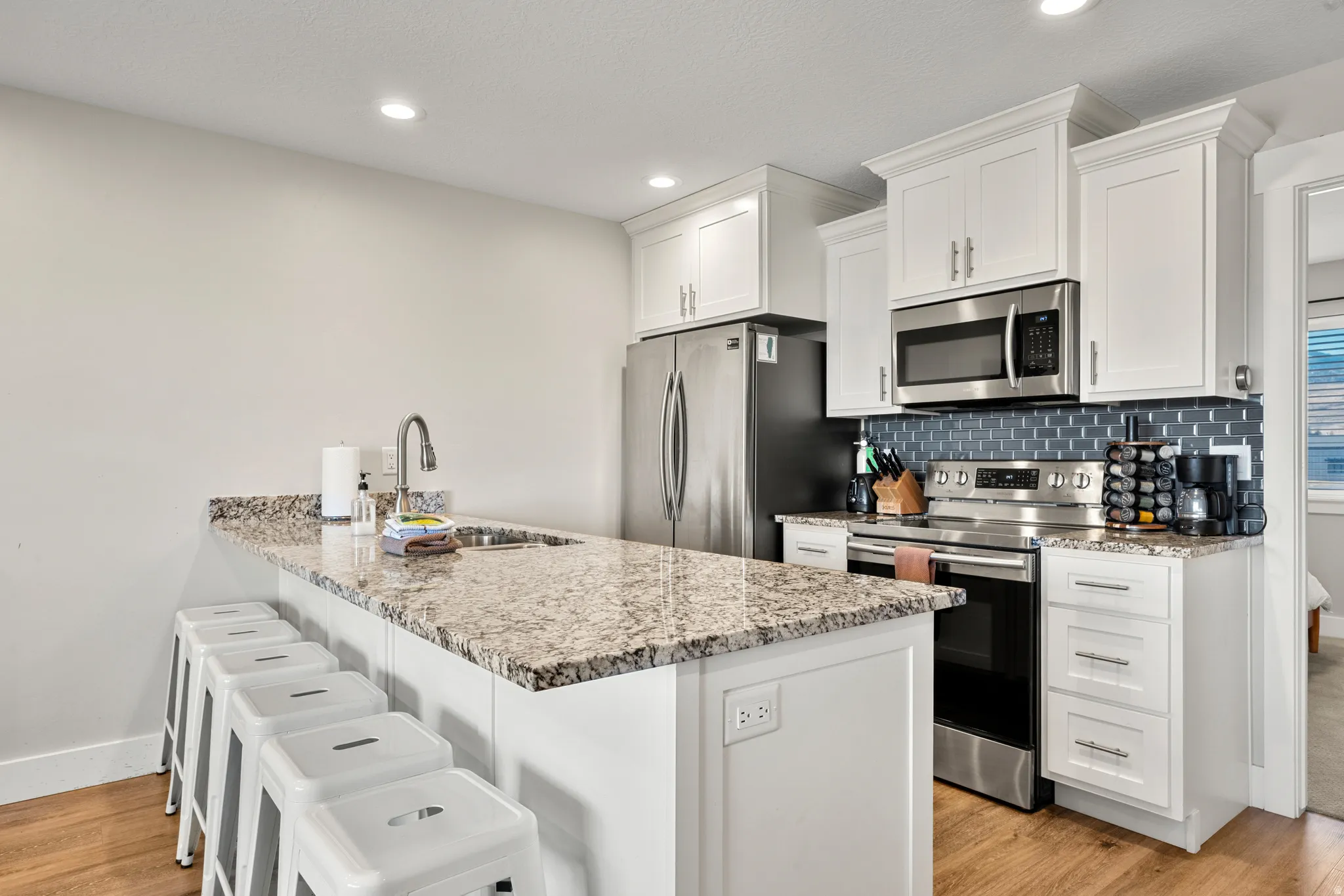 Kitchen featuring an expansive island with a stainless steel sink, granite countertops, white cabinetry, stainless steel appliances, and a subway tile backsplash